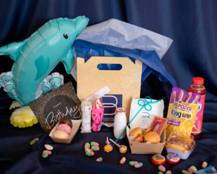 PequeBox de Bizzancio mostrando bollería gourmet, bocados salados, bebidas lácteas y chucherías, todo esto con decoración festiva de fondo. Perfecta para desayunos a domicilio o regalos gourmet para niños.