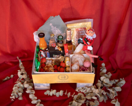 Pedestal Box Edición Navidad Bizzancio con bollería, charcutería y bebidas dulces, todo adornado con un elfo navideño y bastones dulces, ideal como desayuno a domicilio.