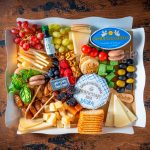 Tabla de Quesos Internacionales Bizzancio con uvas, frutos rojos y macarons en presentación gourmet, ideal como desayuno a domicilio.